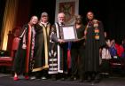 Five people standing on stage at a convocation standing beside one another, as one receives an award.