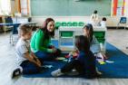 Teacher sitting with kindergarten students on carpet in classroom.