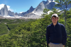 Man standing on a cliff with mountains and forests in the background