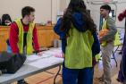 Three volunteers in yellow vests talking around a table in a gymnasium.