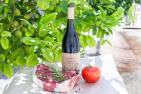 Bottle of wine with a steak and tomato in front.
