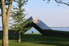 View of park by lakefront with two metal beams coming out of ground (sculpture).