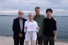 Three men and one woman standing on a pier holding a certificate.