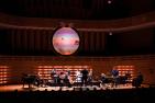 A band playing on a dimly lit stage with an orb-like screen handing above them.