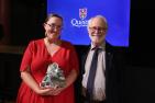 A woman in a red dress holding an award with the man who presented her with it.