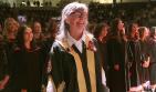 Woman in regalia smiling with students behind her in regalia. 