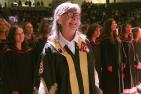 Woman in regalia smiling with students behind her in regalia. 