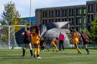 Students playing field hockey in front of a round wooden building. 