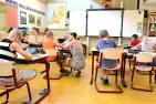 A teacher crouched by a small student's desk, in a classroom.
