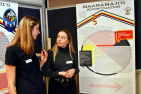 Penny Cornwall (Artsci’18) speaks with Madeline Heinke (Artsci'18) in front of their team's exhibit, Maanamaji'o. The word means "the community (or the person) is sick." (University Communications)