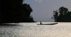 A Brazilian boy in a dugout canoe crosses a river in the evening.