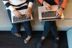 Aerial shot of two pairs of hands working on two laptops. (Photo by Christina Wocintechchat, via Unsplash)
