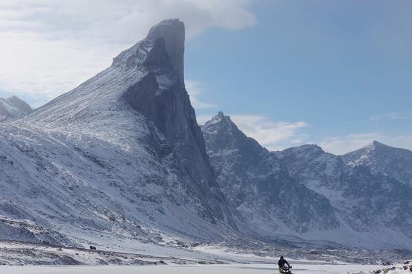 Parks Canada Field Unit member tows qamutiik beneath Thor Peak.