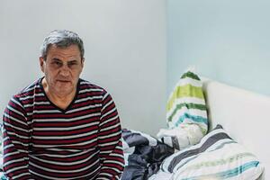 Man in striped shirt sitting on the edge of an unmade bed