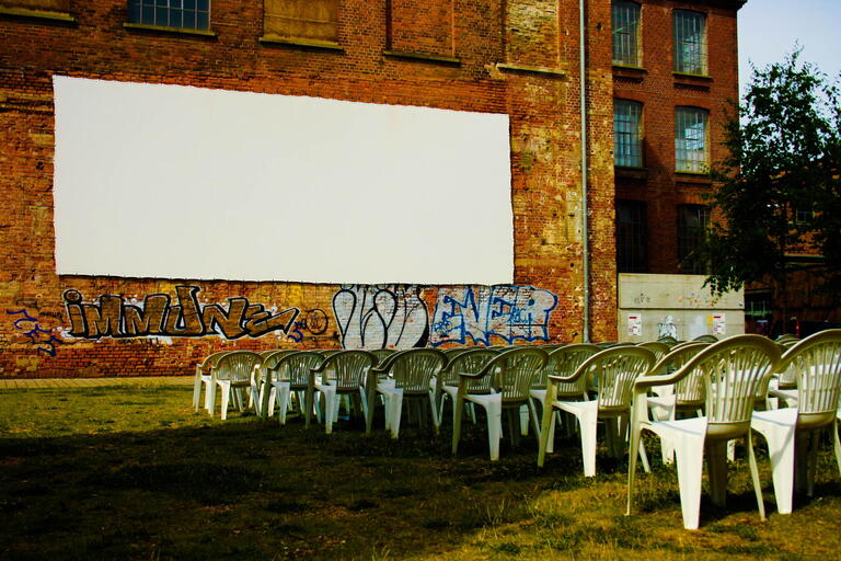 A wall with a screen on it and lawn chairs set up in front of it.