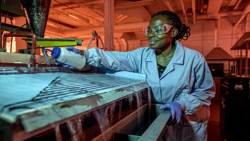 Student wearing a lab coat, exploring and testing liquid in a machine in an industrial setting.