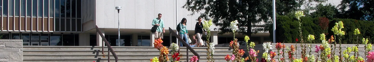 Photo of three people walking down steps outside a modern building with colorful flowers blooming in the foreground.