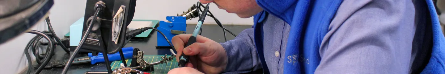 A man focused on assembling electronic components in a well-organized workshop filled with tools and equipment.
