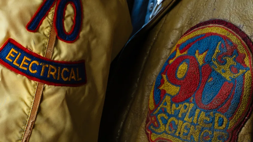 Close-up of vintage jackets displaying embroidered 70th Electrical and Applied Science patches, highlighting engineering tradition and alumni pride.