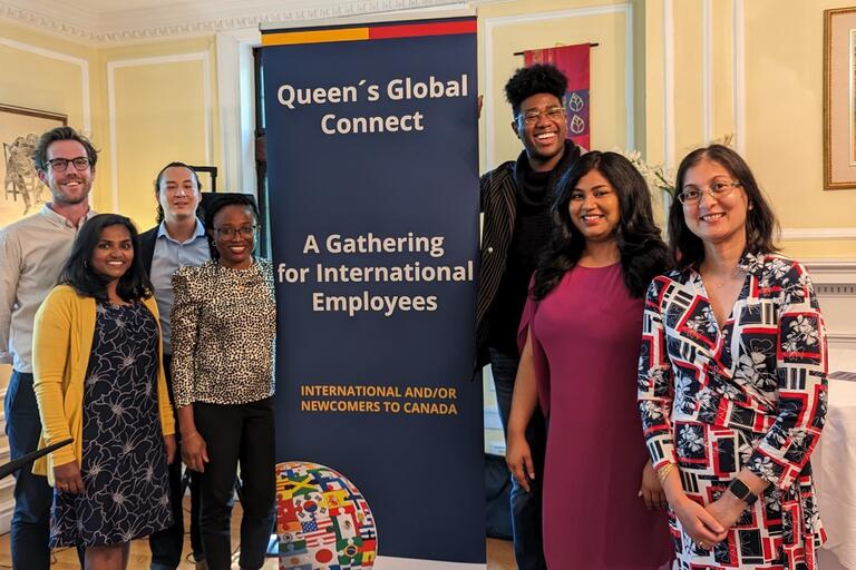 A group of people standing next to a pop-up banner where it reads "Queen's Global Connect"