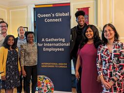 A group of people standing next to a pop-up banner where it reads "Queen's Global Connect"