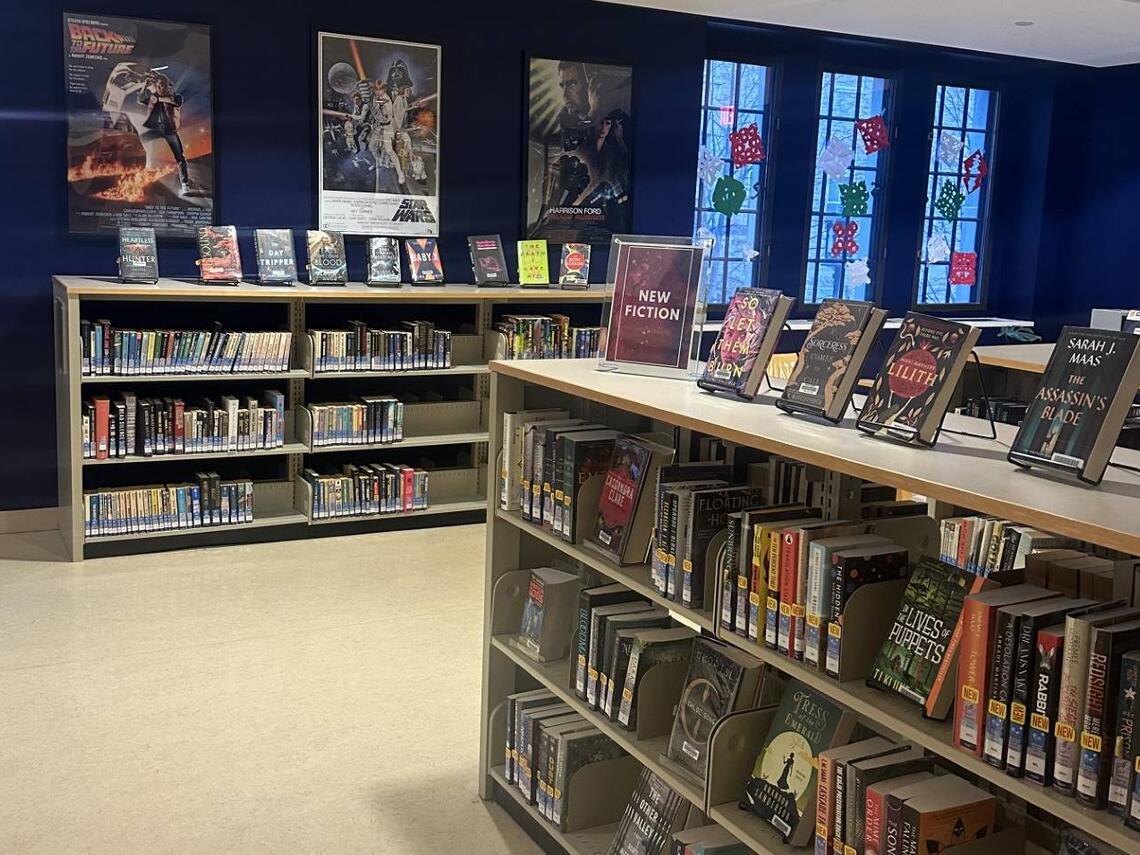 Science fiction section at Douglas Library, Queen’s University, featuring shelves of sci-fi and fantasy books, a “New Fiction” display, classic film posters on blue walls. 