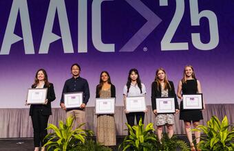 Six young researchers stand on a stage holding framed awards. 