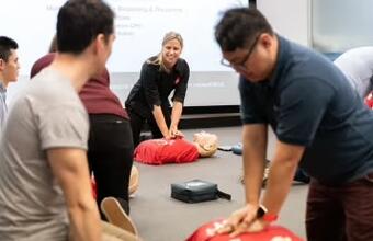 People practicing CPR on manikins in a classroom under instructor guidance.