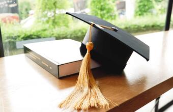 A graduation cap rests against a textbook.