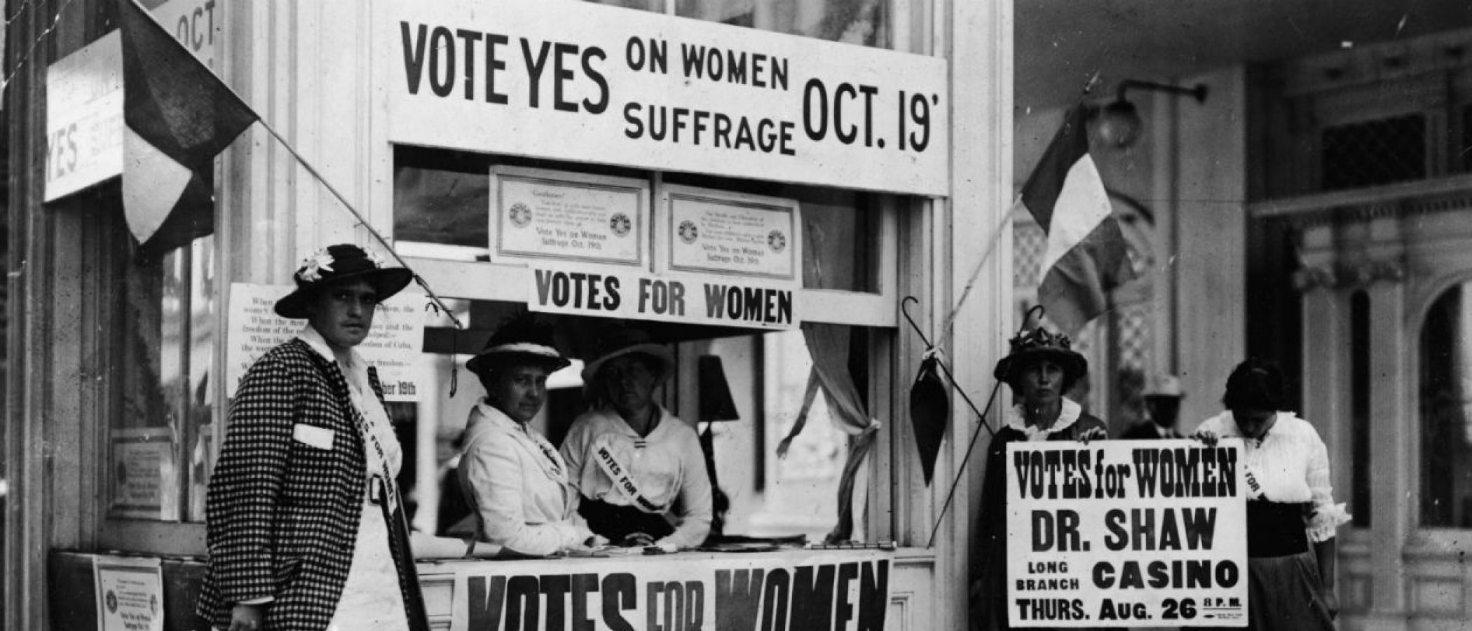 An image of women standing at a booth protesting for women suffrage