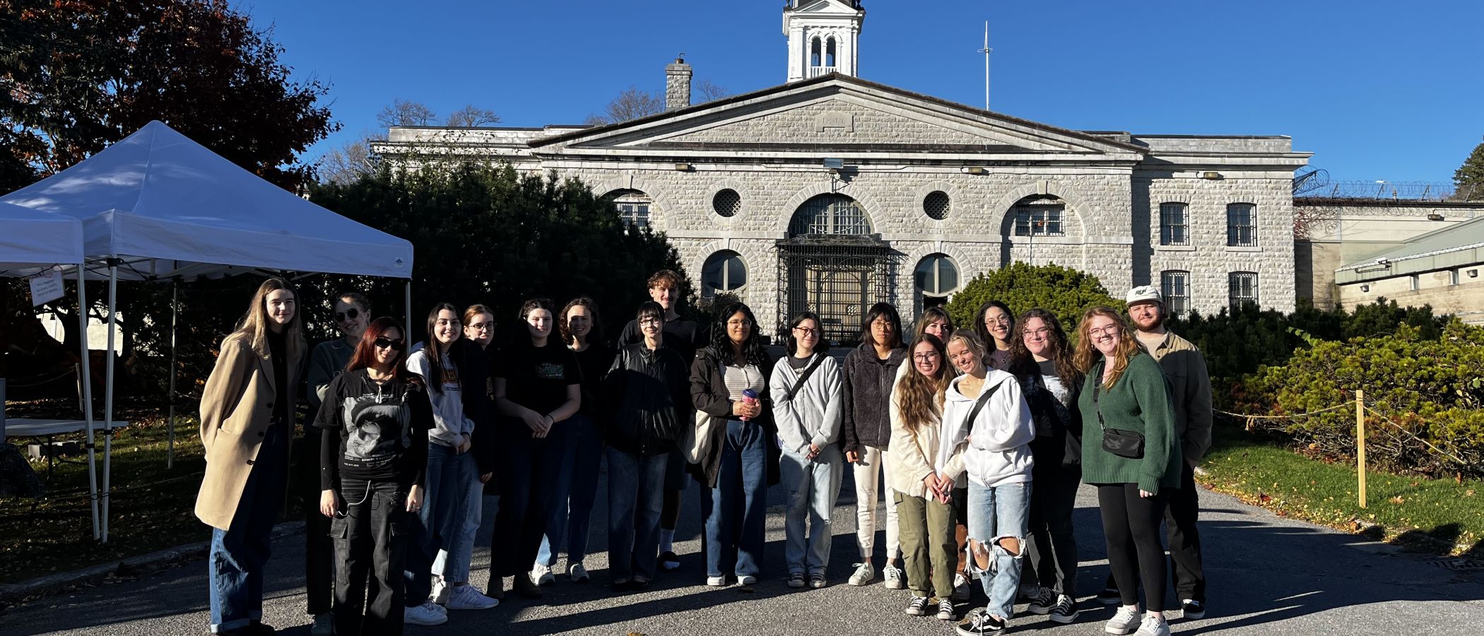 A group of students stands in front of a large stone building on a sunny day.