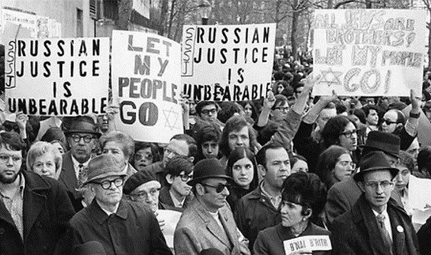 A black and white photograph of protestors holding signs that read "Russian Justice is unbearable" and "let my people go"