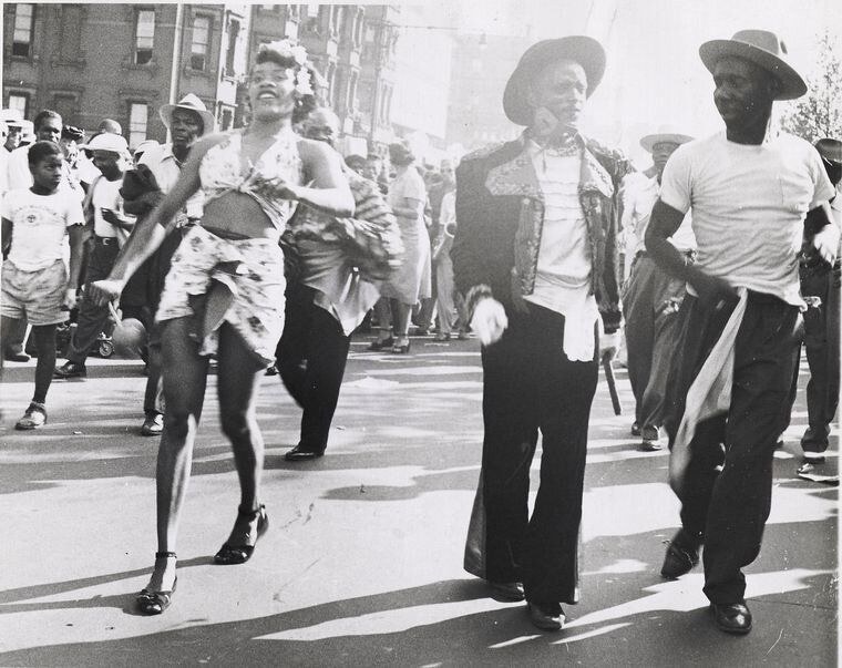 A black and white photograph of men and women parading down a street in the daylight.