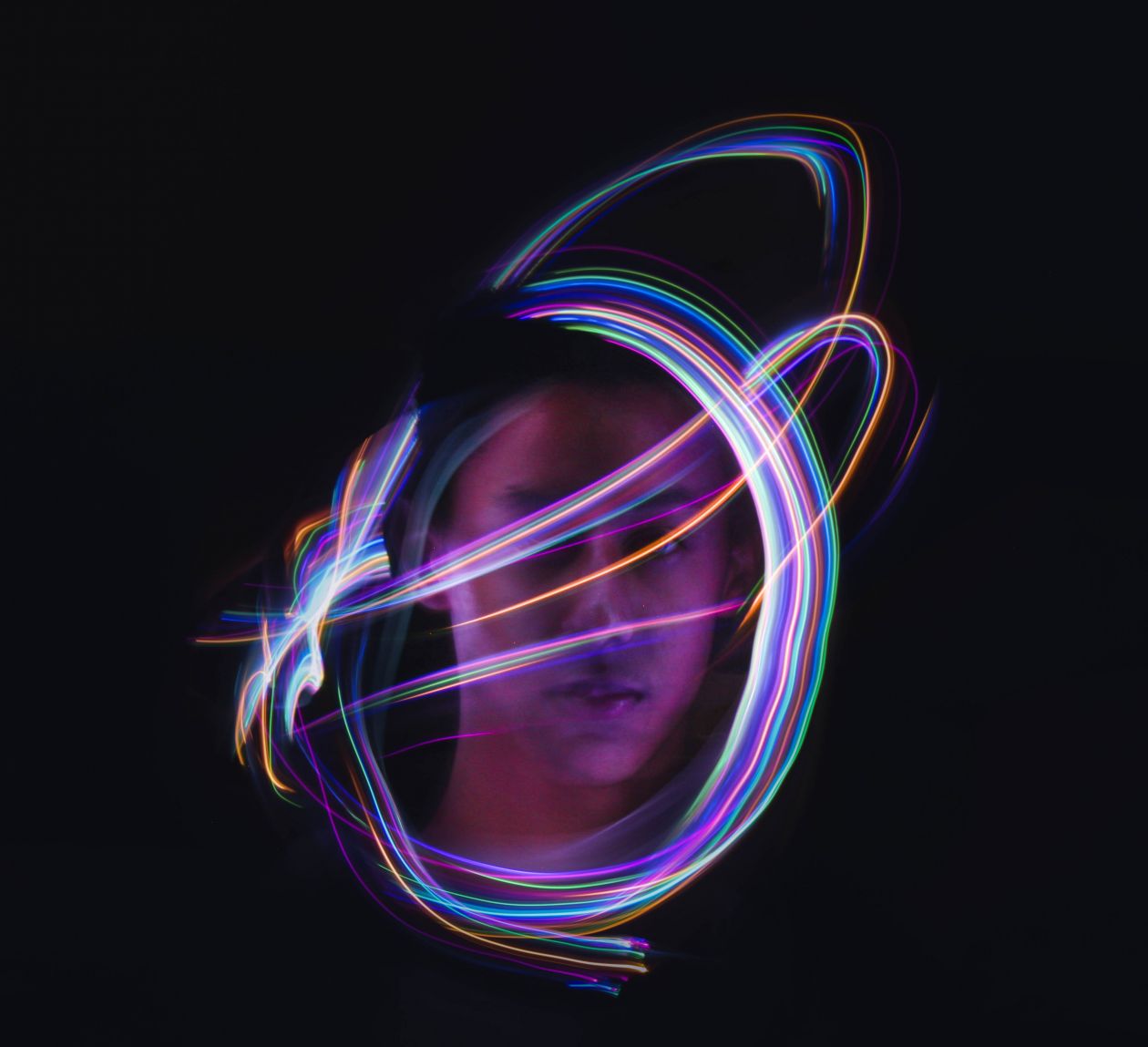 Image of a face on a black background with colourful lights swirling around them