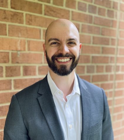 An image of Dagomar Degroot smiling in a blue suit standing in front of a brick wall