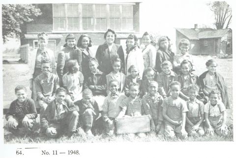 A black and white class photograph of Black school children with their teacher, dated 1948.