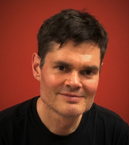 Image of Jeffrey Brison smiling with a red background