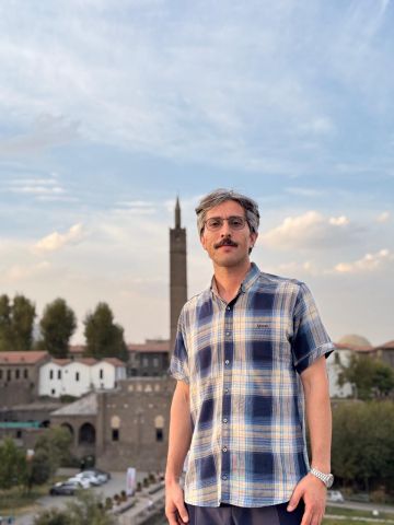 An image of Morad in a plaid shirt standing in front of a historic building