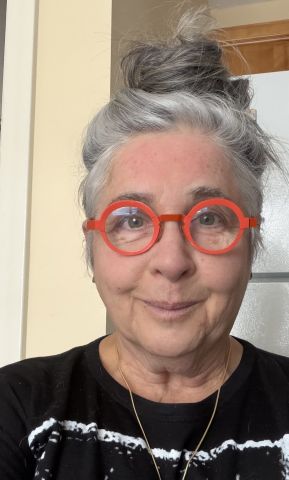 A photo of a woman with grey hair in a bun wearing orange round glasses