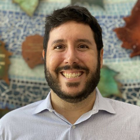 Photograph of a person with black hair and a beard smiling wearing a dress shirt