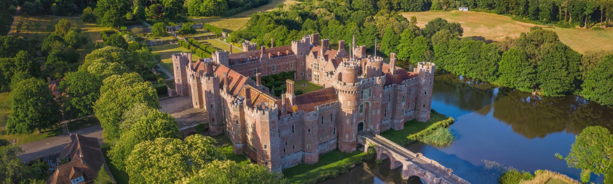 An aerial image of Herstmonceux Castle in a forested area with a pond and a red brick castle