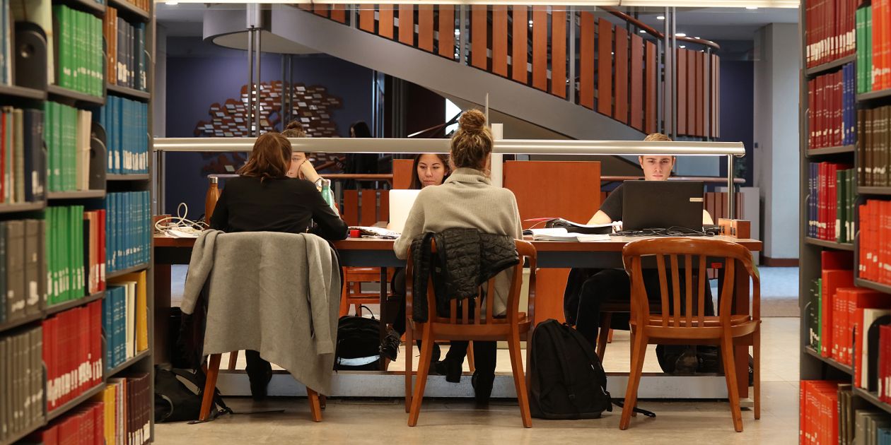 An image of students studying in stauffer library, sitting at a table in wooden chairs