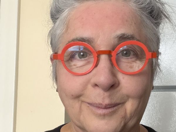 A photo of a woman with grey hair in a bun wearing orange round glasses