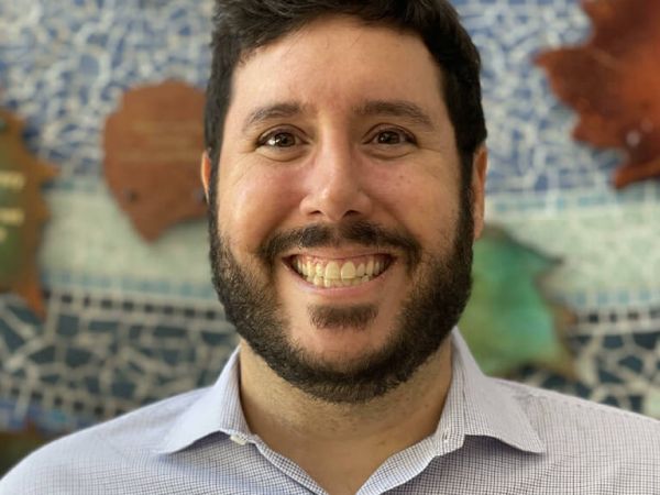 Photograph of a person with black hair and a beard smiling wearing a dress shirt