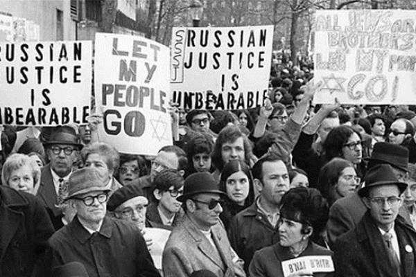 A black and white photograph of protestors holding signs that read "Russian Justice is unbearable" and "let my people go"