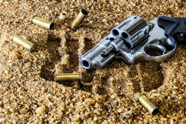 Image of a gun sitting on sand with bullet casings around