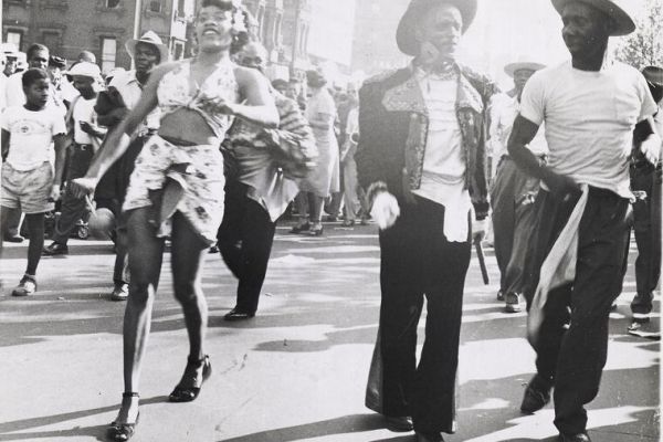 A black and white photograph of men and women parading down a street in the daylight.