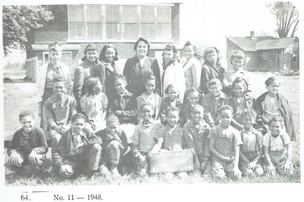 A black and white class photograph of Black school children with their teacher, dated 1948.