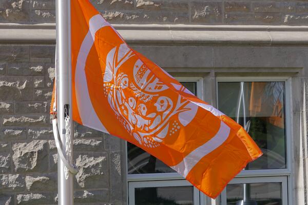 [orange and white flag on flag pole in front of grey brick building]