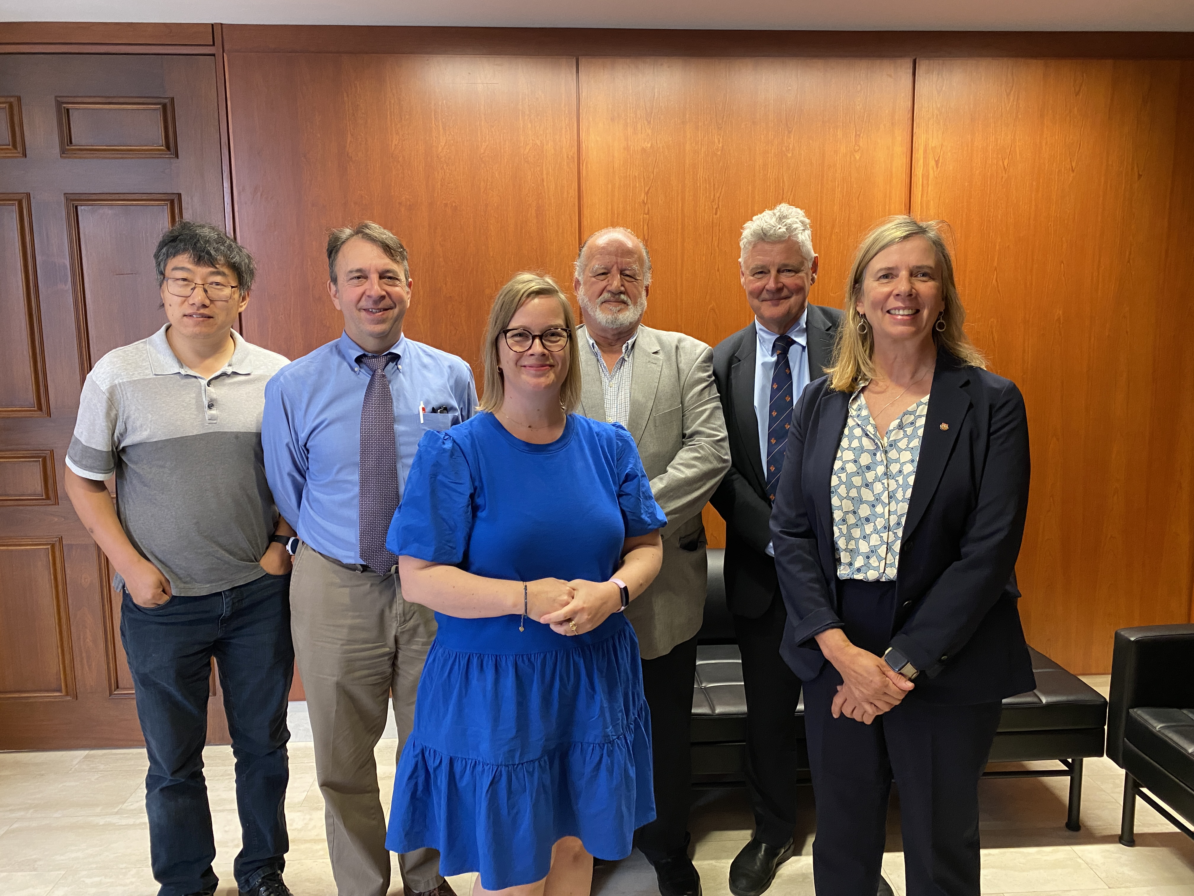 A group photo of six individuals, including Dr. Li, Dr. Stoner, Dr. Macdonald, Dr. Hunter, Dr. den Otter, and Dr. El-Fawal standing in front of a wood wall.